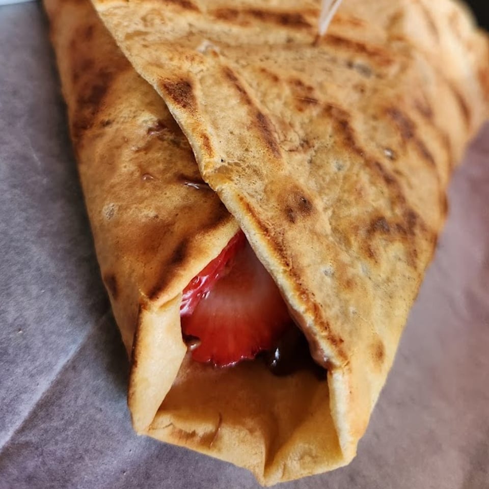 A golden-brown crepe from Crepes Café, filled with sliced strawberries and chocolate sauce.