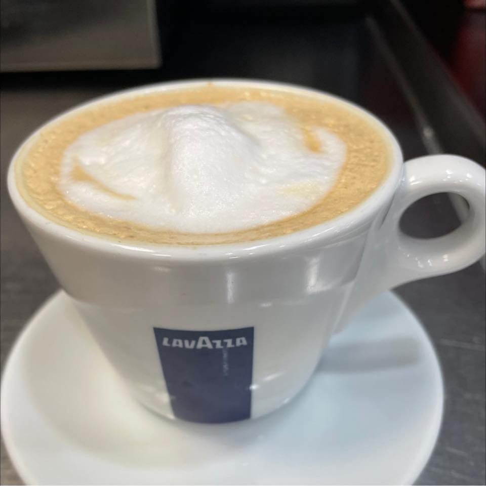 A white Lavazza cup filled with a cappuccino, topped with thick white foam, on a saucer.
