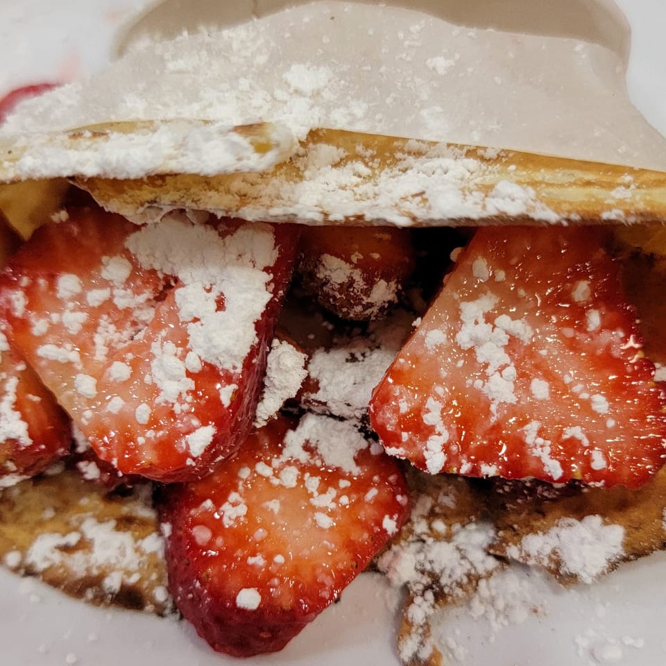 Crepes Café strawberry crepe, folded and dusted with powdered sugar, revealing fresh strawberry slices.