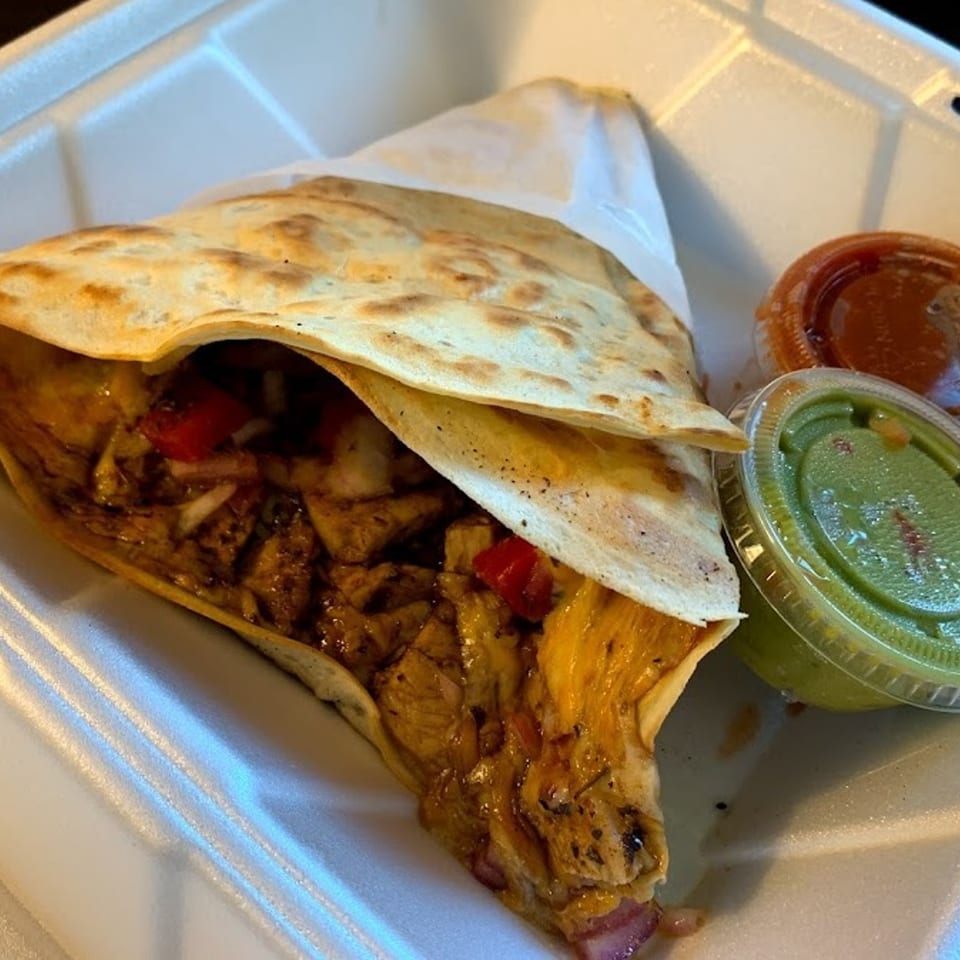 Savory crepe filled with meat, cheese, and vegetables, served with guacamole and salsa in a to-go container.